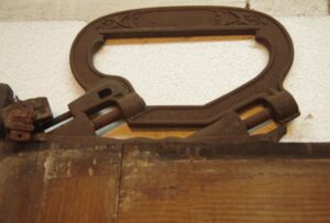 Close-up of a pocket door roller hardware mounted on a dark wood door with distressed wood grain visible.
