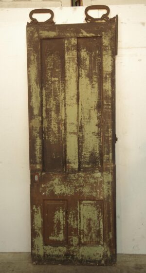 Distressed wood pocket door with four vertical panels and traces of green paint on one side.