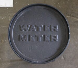 Round side table with a reclaimed cast iron water meter cover top stamped WATER METER.