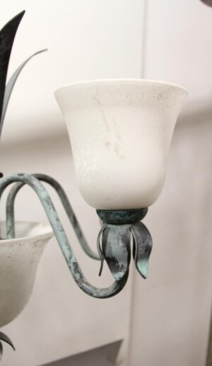 Close-up of a chandelier arm with a white frosted glass shade and green metal leaf detail.