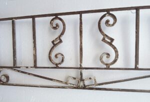 Antique wrought iron window guard with scrollwork and vertical bars, shown with a rusted black finish and sold as is.