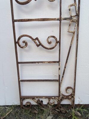 Antique wrought iron window guard with rectangular framing and scrollwork, shown with a rusted black finish and worn paint.