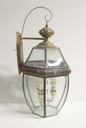 Traditional exterior lantern wall sconce with antique brass trim, clear beveled glass panels, and a hanging hook top.