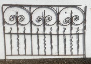 Wrought iron fence section with three fleur-de-lis scroll panels and vertical bars, shown as a small decorative gate or fence piece.