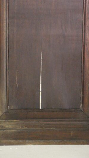 Dark wood wainscot paneling with a carved frame and a central panel showing a vertical seam and minor wear.