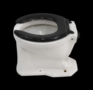 Art Deco toilet bowl with a black seat and white porcelain body, shown in a three-quarter view with surface wear visible.