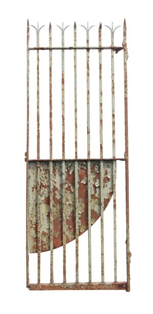 Tall distressed wrought iron gate with split finials and a curved security panel, showing peeling green paint and rust.