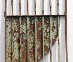Distressed green wrought iron gate with vertical bars, a security panel, and heavily peeling paint that reveals rust beneath.