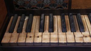 Close-up of an antique piano keyboard with worn wood keys and dark accidentals, shown from above.