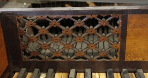 Close-up of an antique piano keyboard with dark wood tone casing and a decorative lattice grille above the keys.