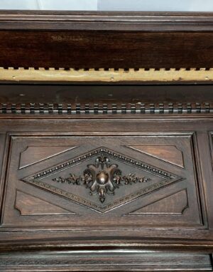 Close-up of a dark wood tone walnut fireplace mantel with ornate Rococo carved panel details and visible reclaimed wear.