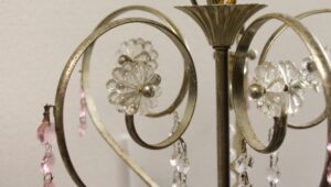 Close-up of a silver chandelier with curved arms, clear glass floret details, and hanging pink crystal bead chains.