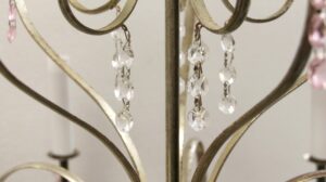 Close-up of a silver-plated chandelier with faceted clear crystal pendants and rose-colored bead chains hanging from curved arms.
