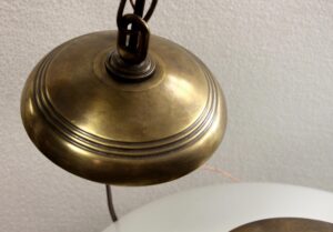 Close-up of a schoolhouse light with an antique brass chain fitter and part of the white milk glass globe visible.