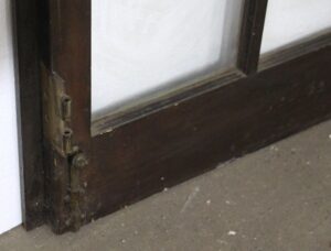 Close-up of a dark wood tone French door showing the hinge side and lower rail detail.