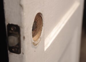 Close-up of a white wooden passage door showing the latch bore and strike plate cutout, with worn edges around the opening and part of the hardware visible on the side.