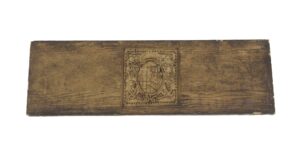 Brown Arts & Crafts pediment with a central coat of arms motif and aged wear.