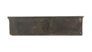 Brown Arts and Crafts pediment with a central coat of arms motif and worn edges.