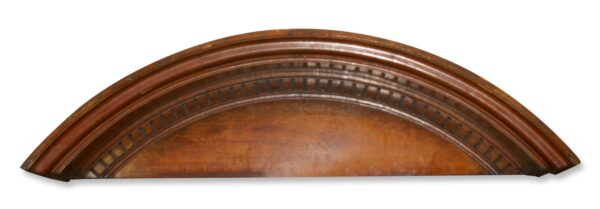 Arched wooden pediment with dentil molding and a curved top profile.