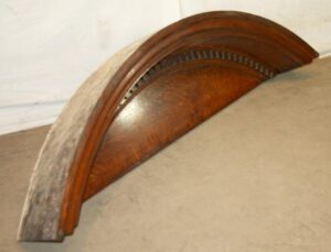 Arched wooden door pediment with dentil molding and a dark wood tone, shown in a close-up view.