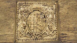 Arts and Crafts pediment panel with a central coat of arms motif, shown in a close-up view with worn brown cast plaster details.
