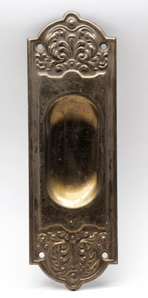 Decorative recessed pocket door plate with an antique brass finish and ornate embossed detailing, shown with four mounting holes and a central pull recess.