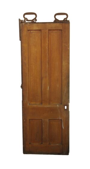 Antique wooden pocket door with four vertical panels, a dark wood tone, and a distressed opposite side with traces of green paint.