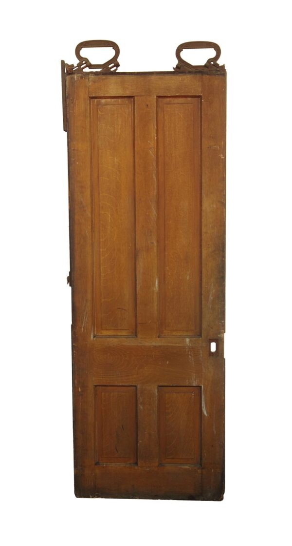 Antique wooden pocket door with four vertical panels, a dark wood tone, and a distressed opposite side with traces of green paint.