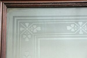 Close-up of a dark wood tone pocket door with an etched glass center panel and decorative border.