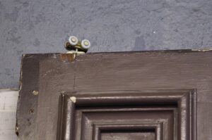 Close-up of a brown pine pocket door showing the top edge, with the six-panel molding partly visible and a small roller hardware piece mounted above it.