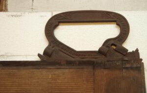 Close-up of the top edge of a dark wood pocket door with an ornate cast-iron handle hardware assembly.