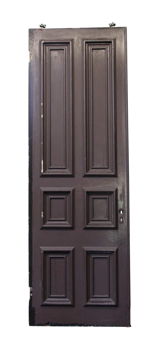Six-panel brown pocket door with thick molded panel detail and visible wear along the edge.