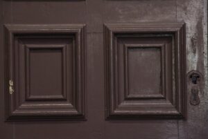 Close-up of a brown six-panel pocket door with thick molding around the panels and visible keyhole hardware on the right side.