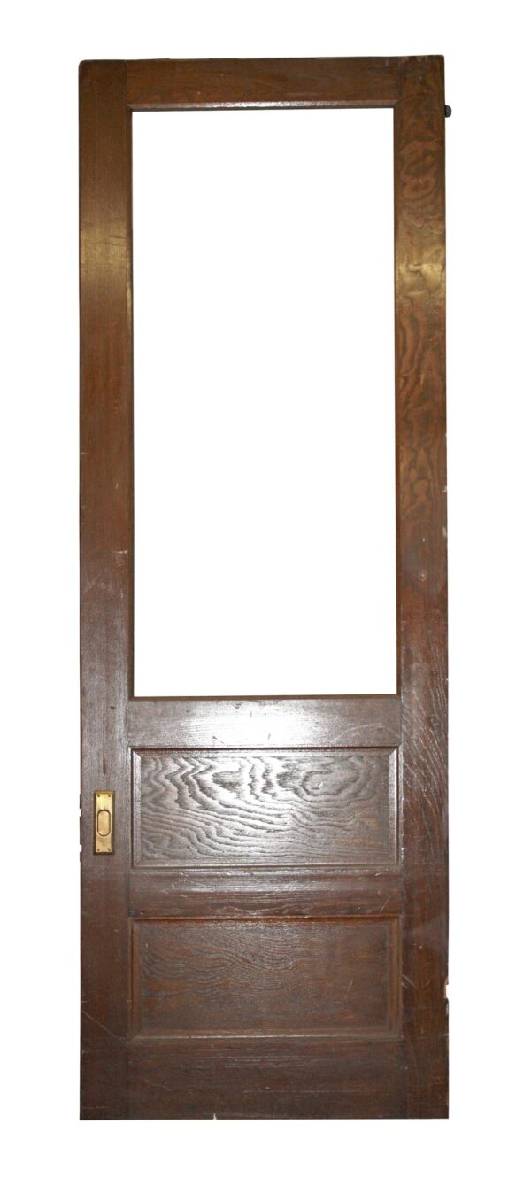 Tall dark wood-tone pocket door with a large upper glass opening, two lower panels, and a brass lock plate on the left side.