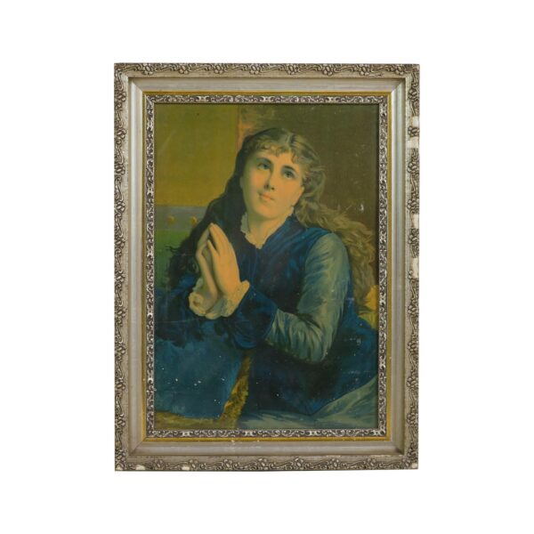 Framed portrait of a young woman kneeling in prayer, shown in an ornate silver frame with visible chipped plaster on the right edge.