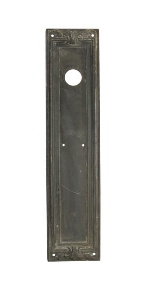 Antique bronze Art Deco door push plate with a central cylinder lock opening and decorative corner detailing.