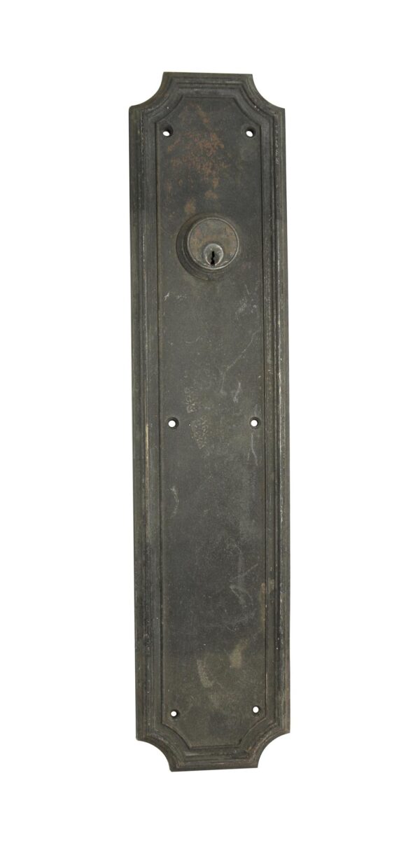 Art Deco bronze push plate with a cylinder lock and four mounting holes, shown in a tall rectangular form with an ornate top and bottom edge.