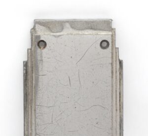 Close-up of a vintage aluminum door push plate showing the back side with two mounting holes and surface wear.