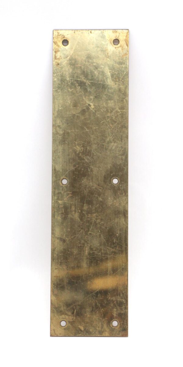 Vertical brass door push plate with four mounting holes and a worn polished brass finish.