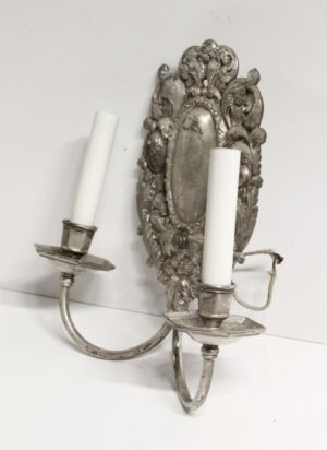 Silver Louis XV rococo two-arm wall sconce with ornate floral and foliage detailing and two candle-style holders.