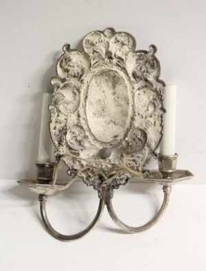 Silvered brass two-arm wall sconce with ornate Rococo floral and foliage detailing and an oval backplate.