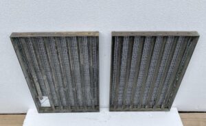 Pair of bronze window grates with woven brass mesh shown side by side, one grate featuring a small cutout in the lower corner.