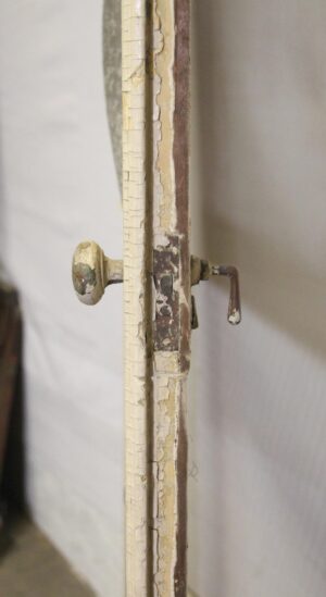 Close-up of a white vintage wood door showing a worn latch and peeling paint on the edge of one panel.