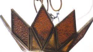 Close-up of a Tiffany style pendant light with faceted stained glass panels in amber, orange, and burgundy tones, showing the pointed shade and visible small breaks in the glass.