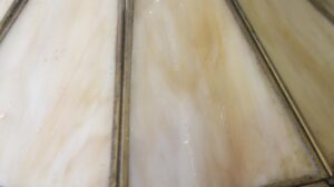 Close-up of a Tiffany-style stained glass pendant light showing amber-toned glass panels with brass dividers and a few small breaks.