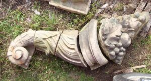 Pair of gray terra cotta cornucopia fragments with carved leaf and scroll details, shown laid out side by side in a close-up view.