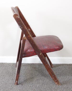 Side view of a folding chair with a bentwood back and a red vinyl cushion.
