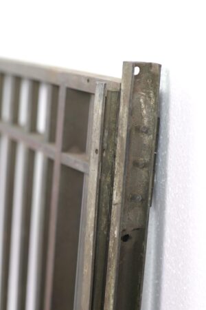 Close-up of an antique bronze bank teller door hinge bracket and latch on the edge of the door.