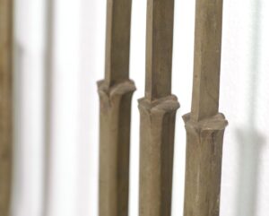 Close-up of brass railing balustrades with an Art Deco profile and antique patina, showing three vertical sections with worn edges and bent details.