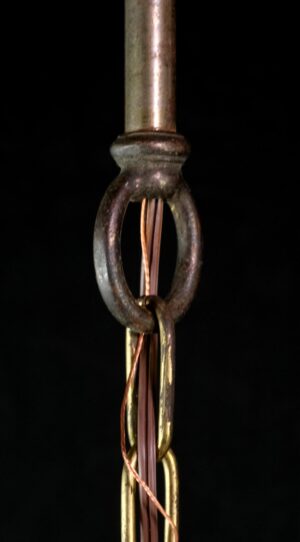 Close-up of a pendant light showing the antique brass fitter and steel chain links attached to the clear glass section.